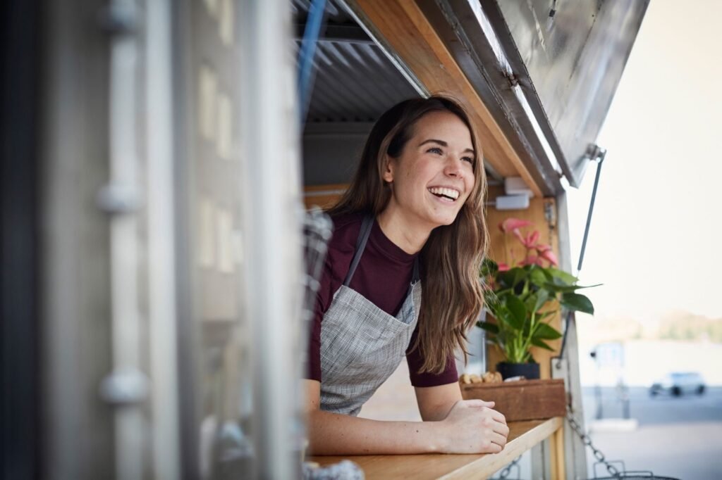 Smiling woman small business owner in apron leaning out of food truck window, representing clients helped by Equal Justice Solutions' small business litigation support program – business litigation lawyer support for small and mission-driven enterprises.